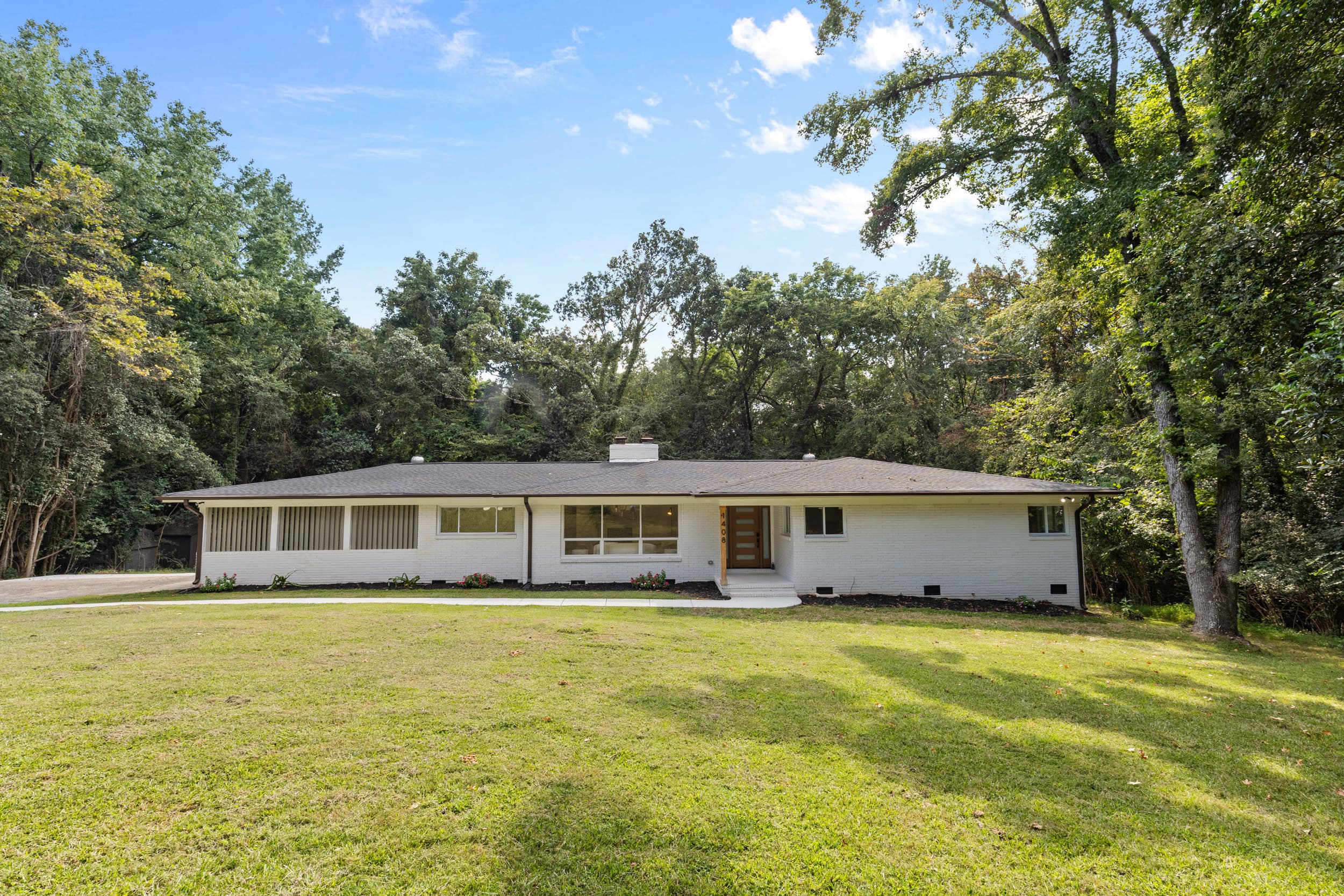 White brick Burtonwood home framed by mature trees and a broad front lawn