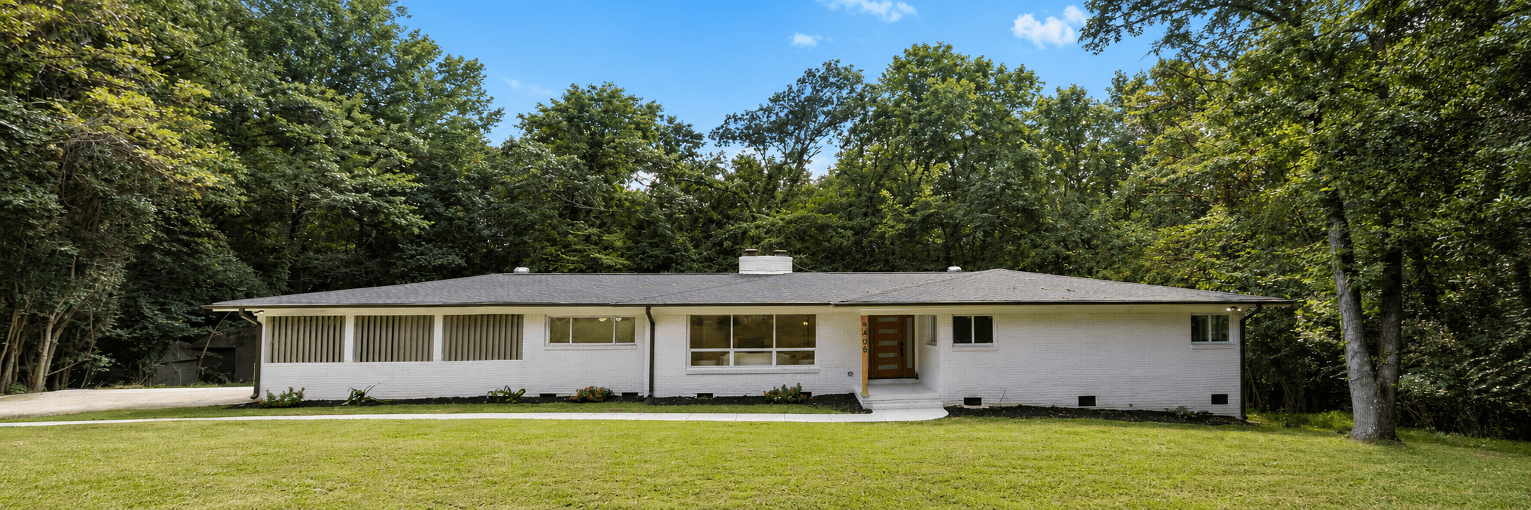White brick Burtonwood home framed by mature trees and a broad front lawn